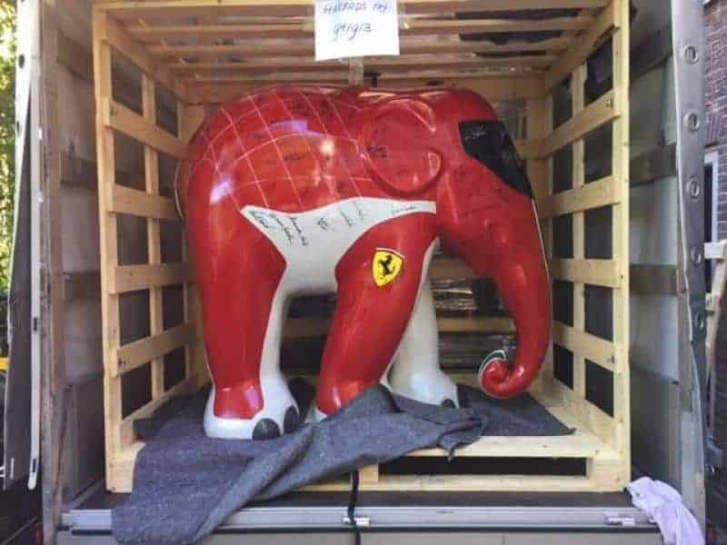 Ferrari Elefant 3 Sztuczny słoń pomalowany w kolorach Ferrari, umieszczony w drewnianej skrzyni transportowej.