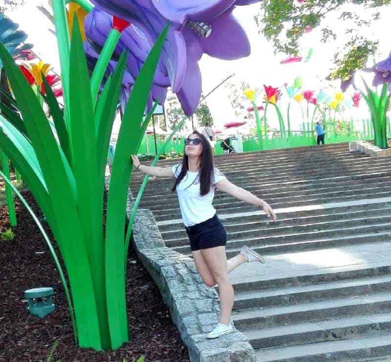 Legendia-Blume 4 Kobieta pozująca przy gigantycznych modelach kwiatów w parku.