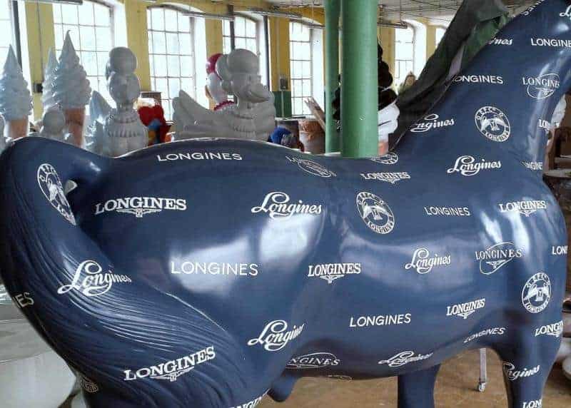 Longines Werbeobjekt 2 Niebieska rzeźba konia pokryta logo marki Longines w hali produkcyjnej.