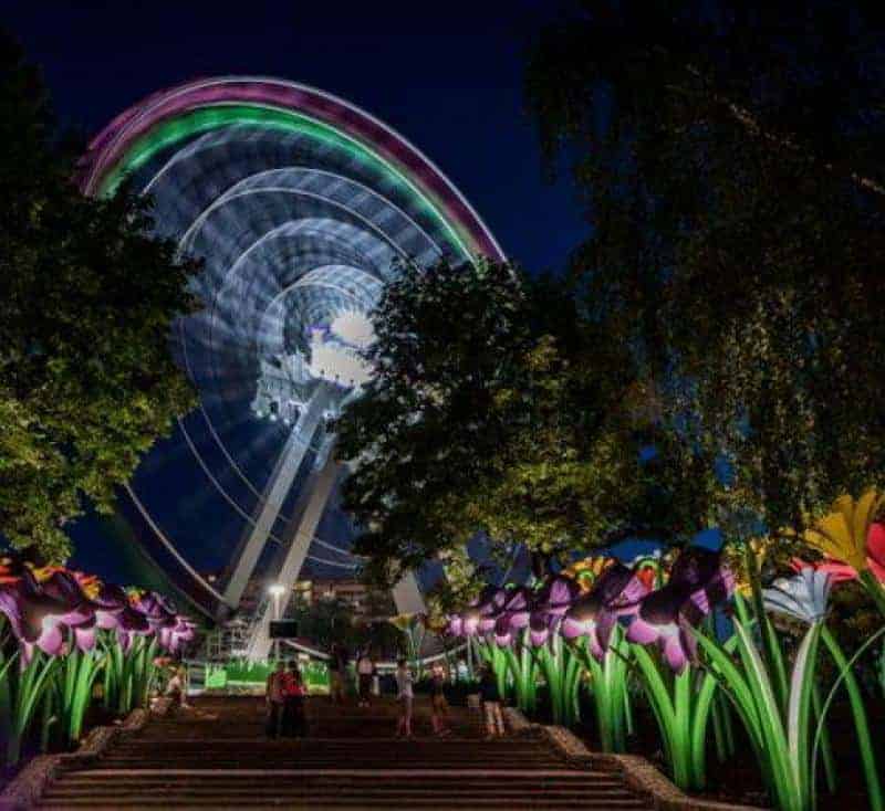 Legendia-Blume 3 Diabelski młyn nocą, otoczony kolorowymi, podświetlonymi kwiatami i drzewami.