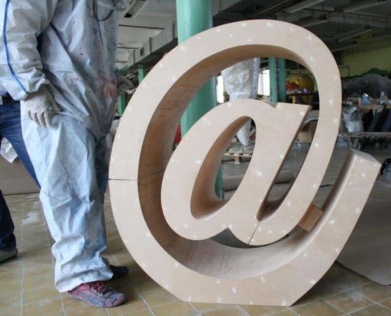 E-Mail-Schreibzeichen 2 Duża rzeźba symbolu małpy (@) w warsztacie, obok której stoi osoba w kombinezonie ochronnym.