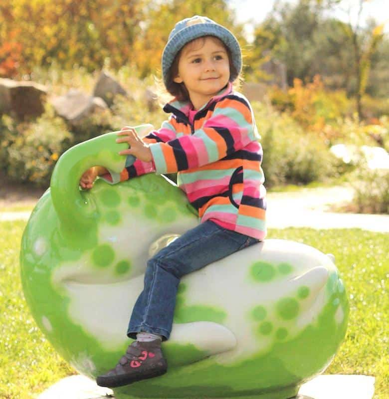 Figuren im Vergnügungspark 4 Dziecko w kolorowej bluzie i niebieskiej czapce siedzi na zielonej huśtawce w kształcie dinozaura na placu zabaw.