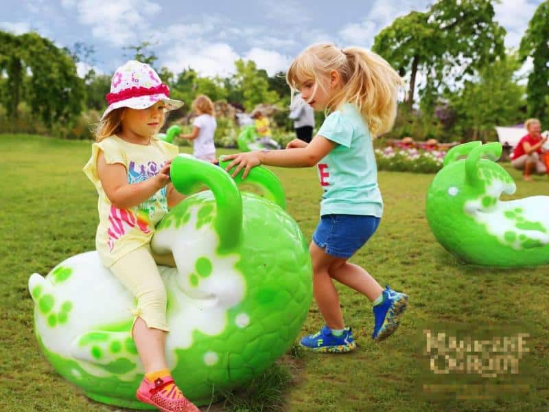 Figuren im Vergnügungspark 1 Dzieci bawiące się na zielonym trawniku z kolorowymi, zielono-białymi, dużymi zabawkami w kształcie ślimaków.