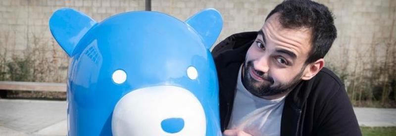 Bär auf einer Bank 3 Mężczyzna obok niebieskiego posągu misia.