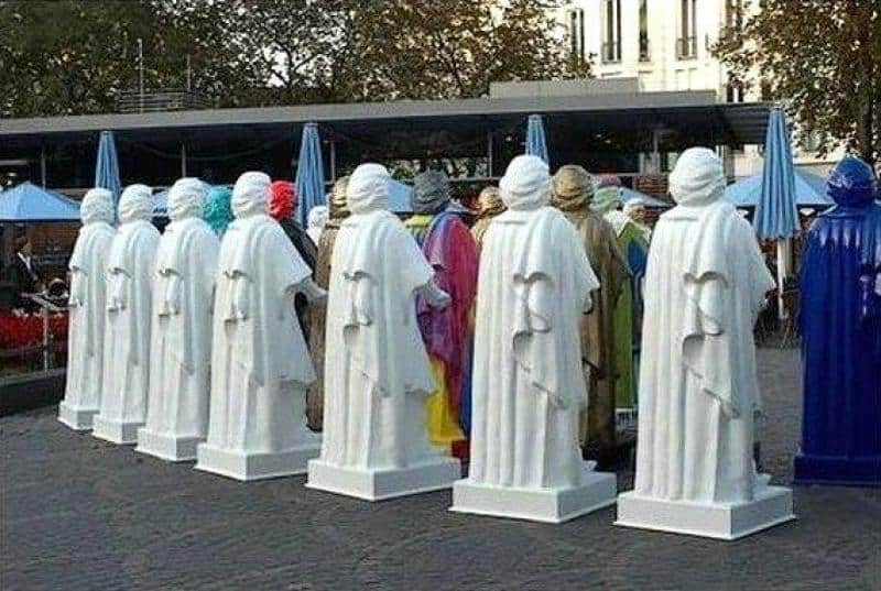 Ludzie przebrani za posągi w białych i niebieskich szatach w parku miejskim.