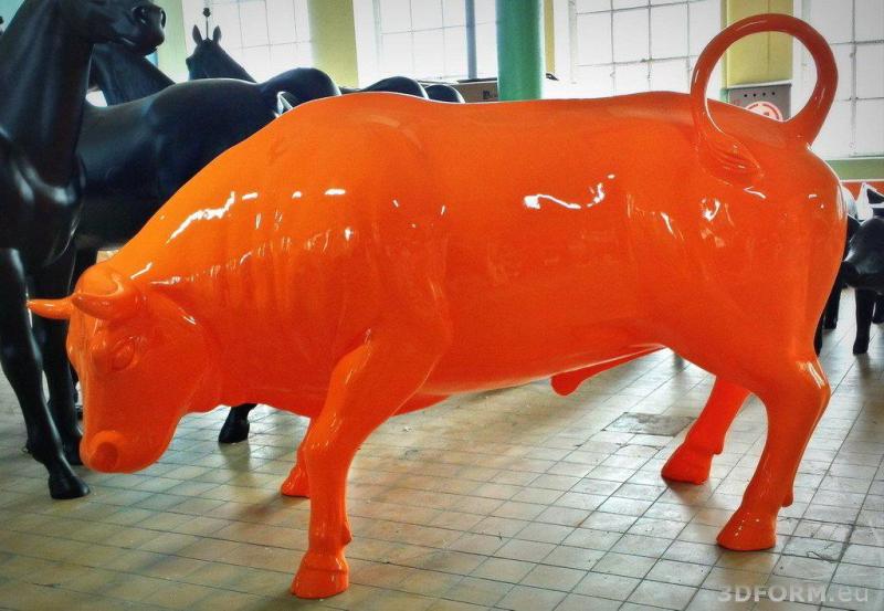 Große Event-Stierfigur 1 Pomarańczowa rzeźba byka znajdująca się w środku, na tle czarnych rzeźb koni