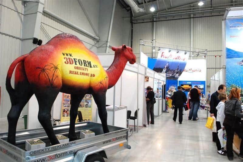 Mobile Kamel-Modell 4 Stoisko wystawowe z dużą figurą wielbłąda promującą obiekty reklamowe 3D; w tle kilka stoisk z banerami i ludzie oglądający ekspozycje.
