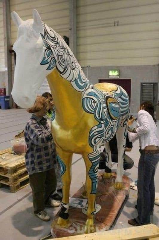 Große Figuren, von Kindern bemalt 3 Ludzie malujący dużą rzeźbę konia w budynku.