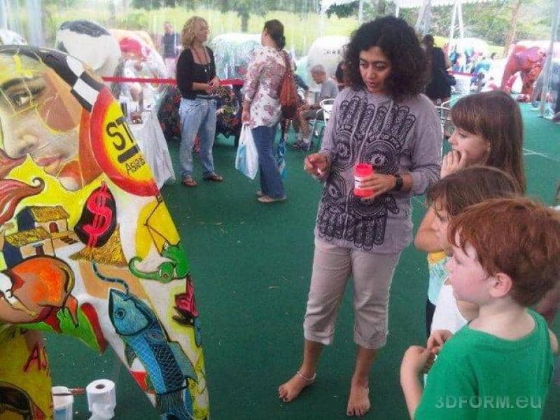 Große Figuren, von Kindern bemalt 2 Kobieta i dzieci stojące przed kolorowym muralem na wystawie plenerowej.