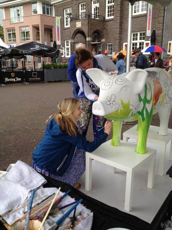 Große Figuren, von Kindern bemalt 1 Kobiety malują wielką rzeźbę krowy na zewnątrz budynku.