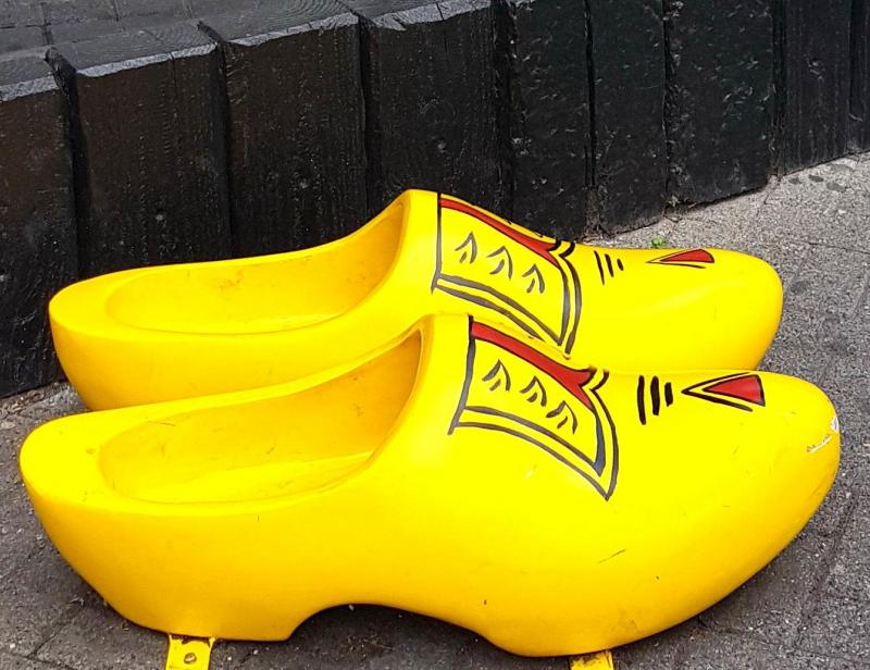 Große Holzschuhe 2 Żółte drewniaki z czerwono-czarnym wzorem, stojące na chodniku przy murze.