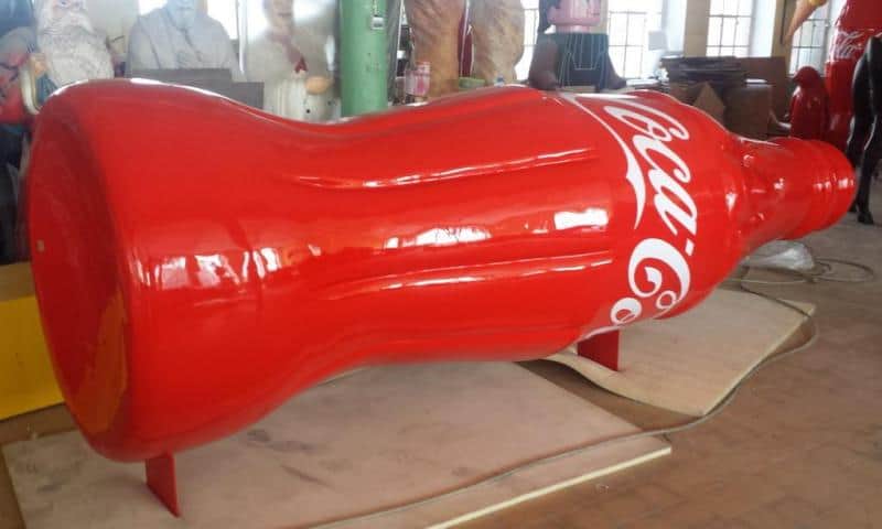 Werbetruck von Coca Cola 2 Duża rzeźba w kształcie butelki Coca-Coli w czerwonym kolorze, znajdująca się w warsztacie.