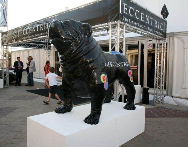 Czarna rzeźba psa na białym postumencie przed wejściem na wydarzenie 