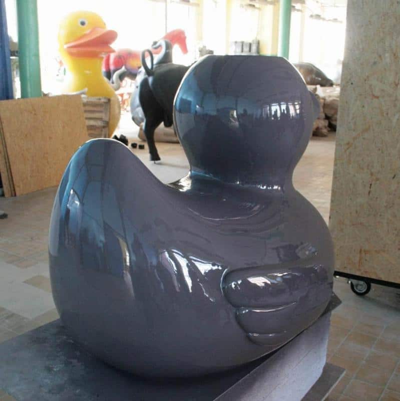 Festivalattraktionen 3 Duża, szara rzeźba kaczki w warsztacie z większymi rzeźbami w tle, w tym żółtą kaczką.