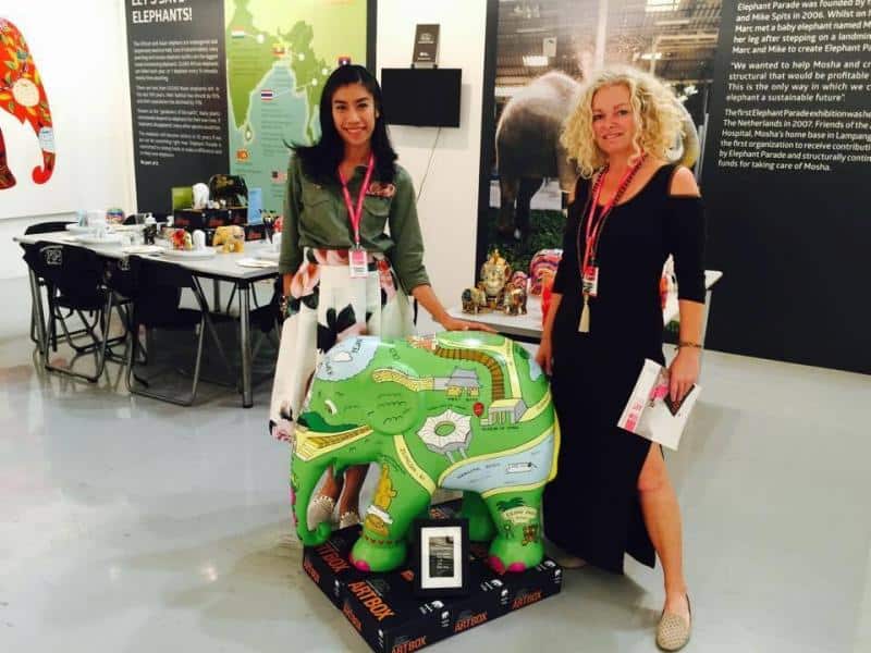 Elefantenparade 2 Dwie kobiety stojące obok kolorowej figurki słonia, trzymające broszury na tle wystawy.