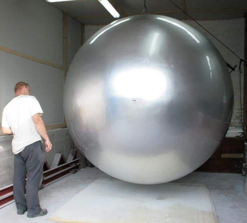Große Kugel im Stadtbereich 4 Mężczyzna stojący obok ogromnej, srebrnej kuli w hangarze.
