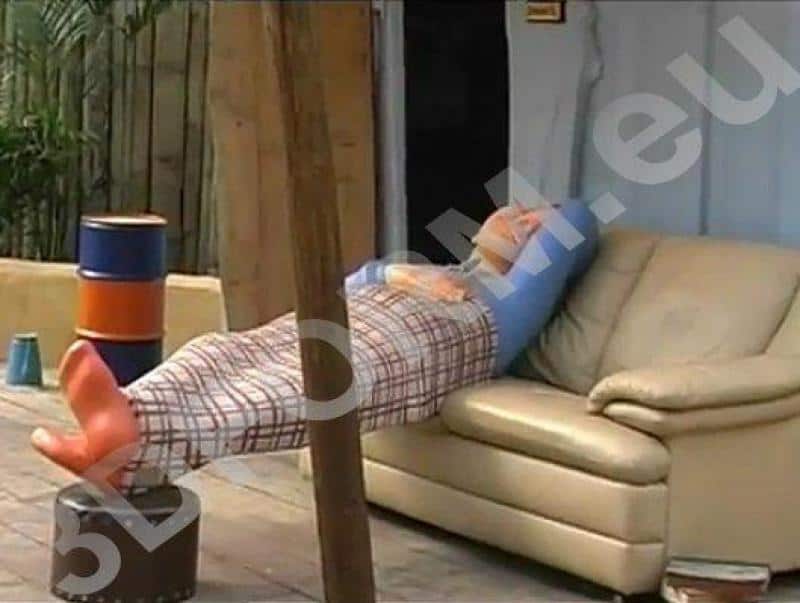 Mężczyzna leżący na kanapie na świeżym powietrzu, przykryty kocem, jego nogi podparte na beczce.