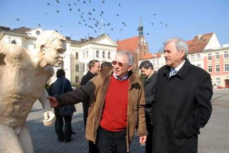 Werbung für die IAAF-Weltmeisterschaften 1 Dwóch mężczyzn rozmawiających obok rzeźby na rynku miejskim, w tle kamienice i wieża zegarowa.