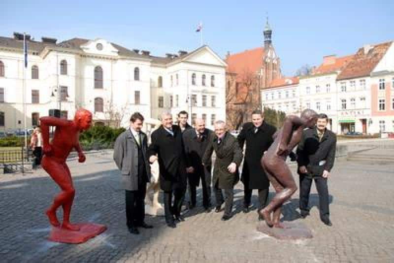 Werbung für die IAAF-Weltmeisterschaften 3 Grupa mężczyzn na placu z rzeźbami w mieście z budynkami w tle.