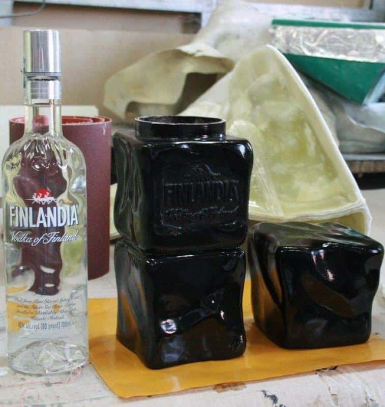 Promotionsverpackung Finlandia 2 Butelka Finlandia Vodka To/1750 ml oraz trzy czarne, zdeformowane butelki Finlandia umieszczone na stole roboczym.