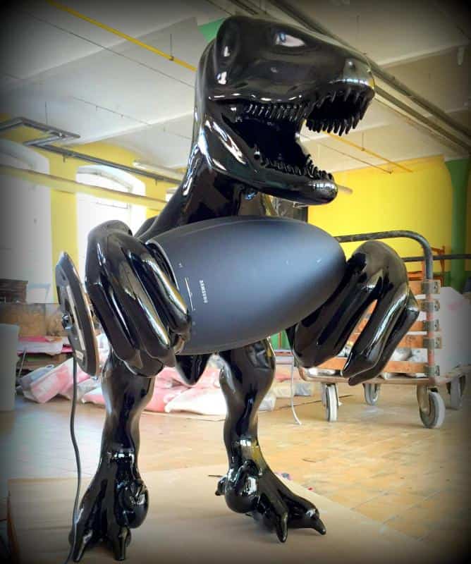 Samsung /KaDeWe / Berlin 3 Rzeźba błyszczącego czarnego dinozaura trzymającego duży głośnik w jasnym pomieszczeniu.