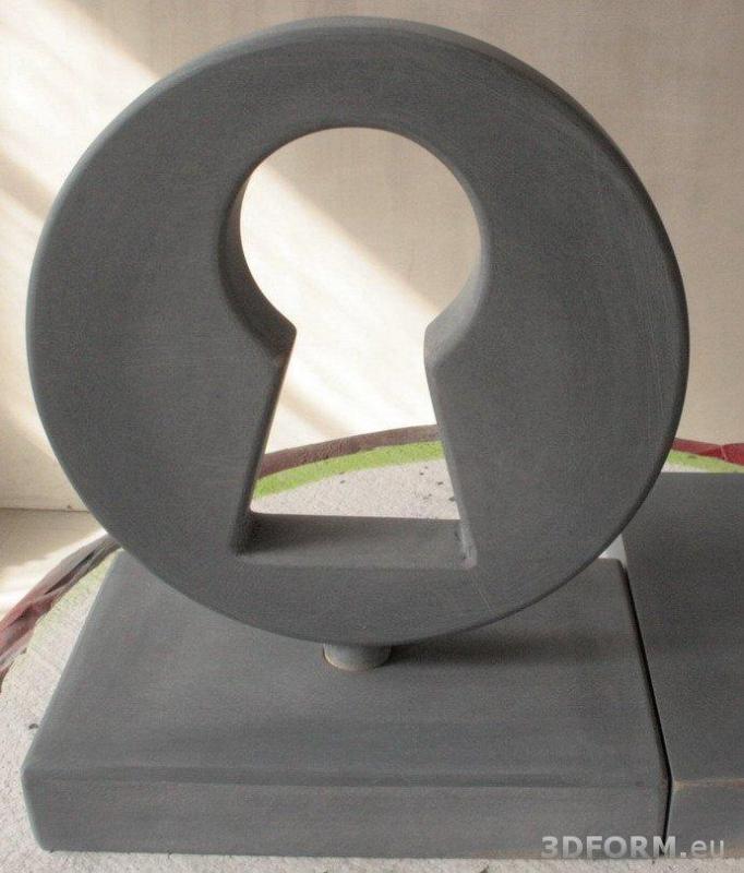 Schlüsselloch / Statuette 2 Szara rzeźba w kształcie zamka do klucza, umieszczona na prostokątnej podstawie.