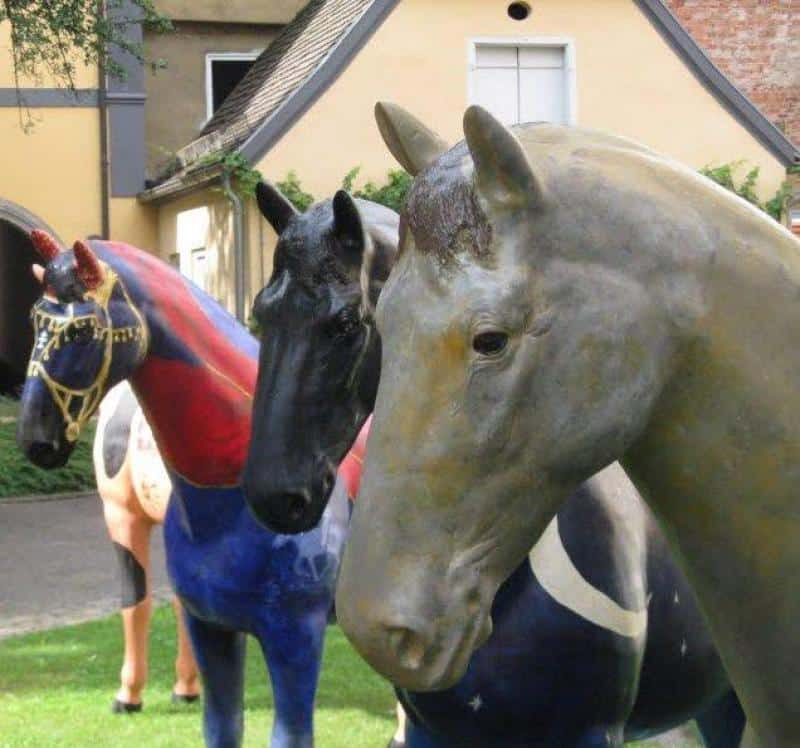 Event-Pferdefiguren 4 Trzy kolorowe rzeźby koni ustawione w ogrodzie przed domem.