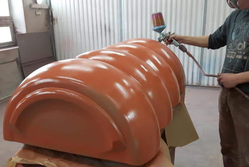 Osoba malująca pistoletem natryskowym duży, pomarańczowy element.