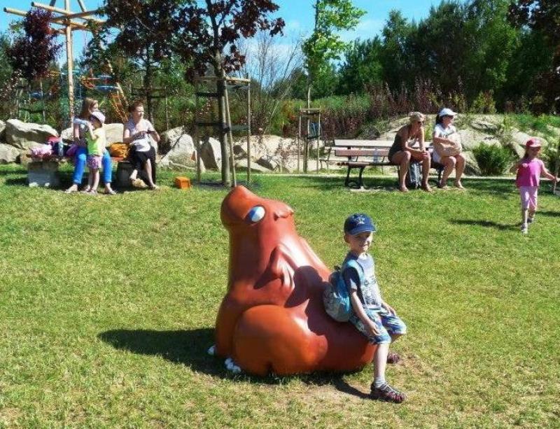 Drachen im Vergnügungspark 3 Chłopiec siedzący na rzeźbie zwierzęcia w parku, w tle kilka osób i drzewa.