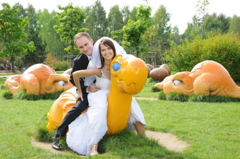 Drachen im Vergnügungspark 2 Para młoda siedząca na dużej, pomarańczowej figurce zwierzęcia w parku.