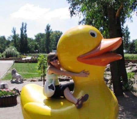 Figuren in einem Themenpark 3 Osoba obejmująca dużą plastikową żółtą kaczkę w parku.