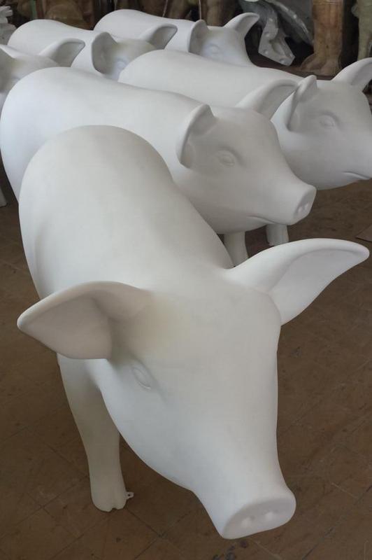 Künstlerisch bemalte Tierfiguren 3 Białe figury świń ustawione jedna za drugą na drewnianej podłodze.