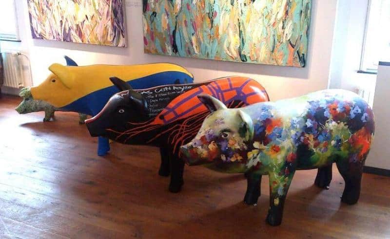 Künstlerisch bemalte Tierfiguren 1 Trzy kolorowe rzeźby świni w galerii sztuki, każda ozdobiona różnorodnymi wzorami i malowidłami.