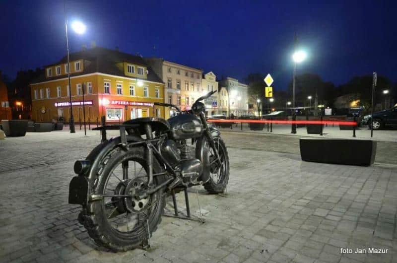 Ikonisches Motorrad - Denkmal in Żagań 4 Motocykl na placu miejskim nocą, w tle oświetlone kamienice.