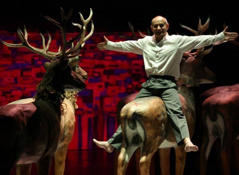 Bühnenbild-Elemente für das Dramatische Theater der Hauptstadt Warschau 4 Mężczyzna siedzący na makiecie jelenia na scenie z czerwono-fioletowym tłem.