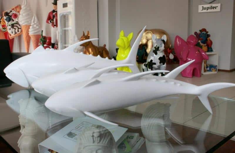 Białe figurki rekinów na szklanym stole, w tle kolorowe figurki zwierząt i inne dekoracje.