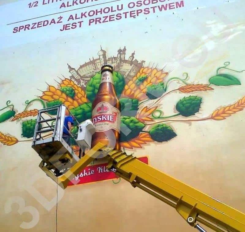 Dreidimensionales Wandbild TYSKIE 2 Osoba na podnośniku malująca reklamę piwa Tyskie na ścianie budynku.
