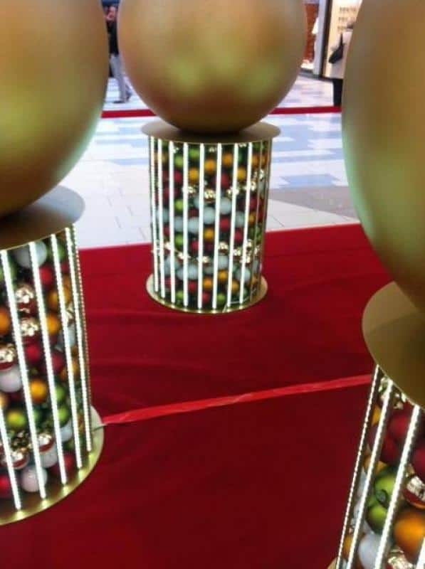 Beleuchtete Weihnachtskugeln 3 Duże złote kule na cylindrycznych stojakach w galerii handlowej.