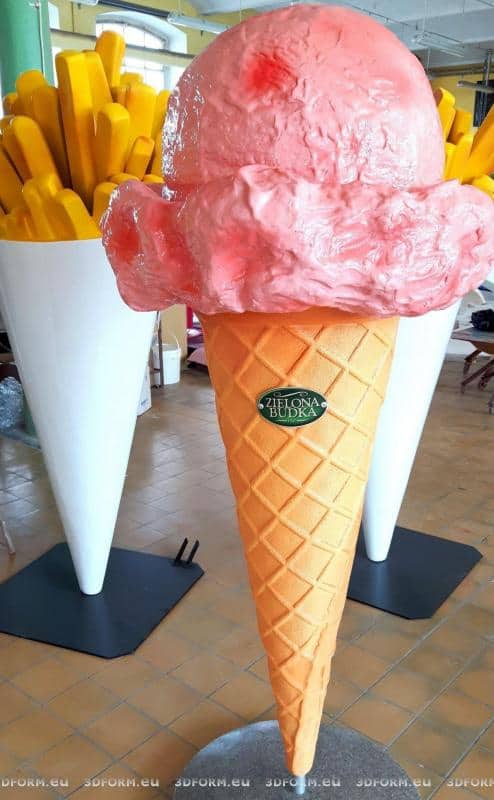 Duży model lodów w rożku z różową gałką oraz duży model frytek w białym kubełku, w tle.