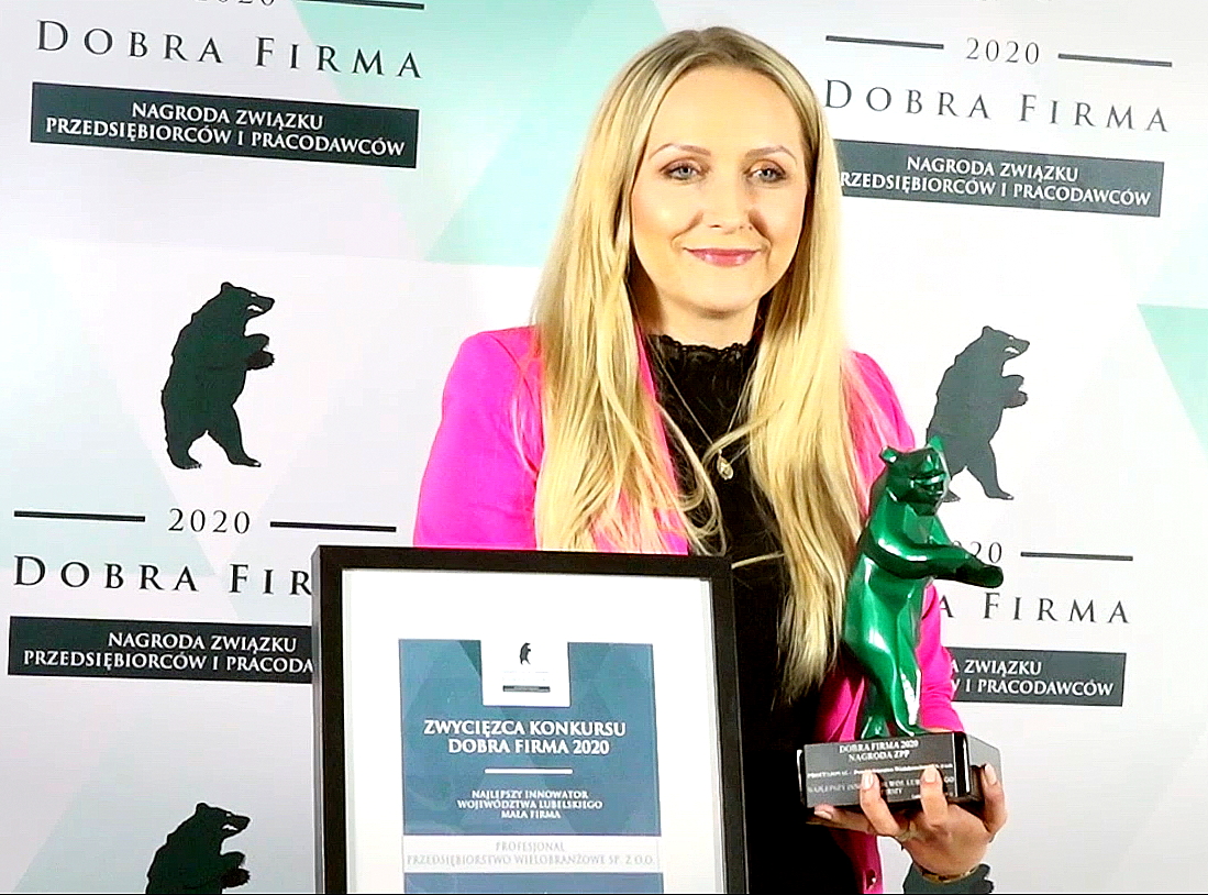 Kobieta w różowej marynarce trzyma nagrodę oraz certyfikat 