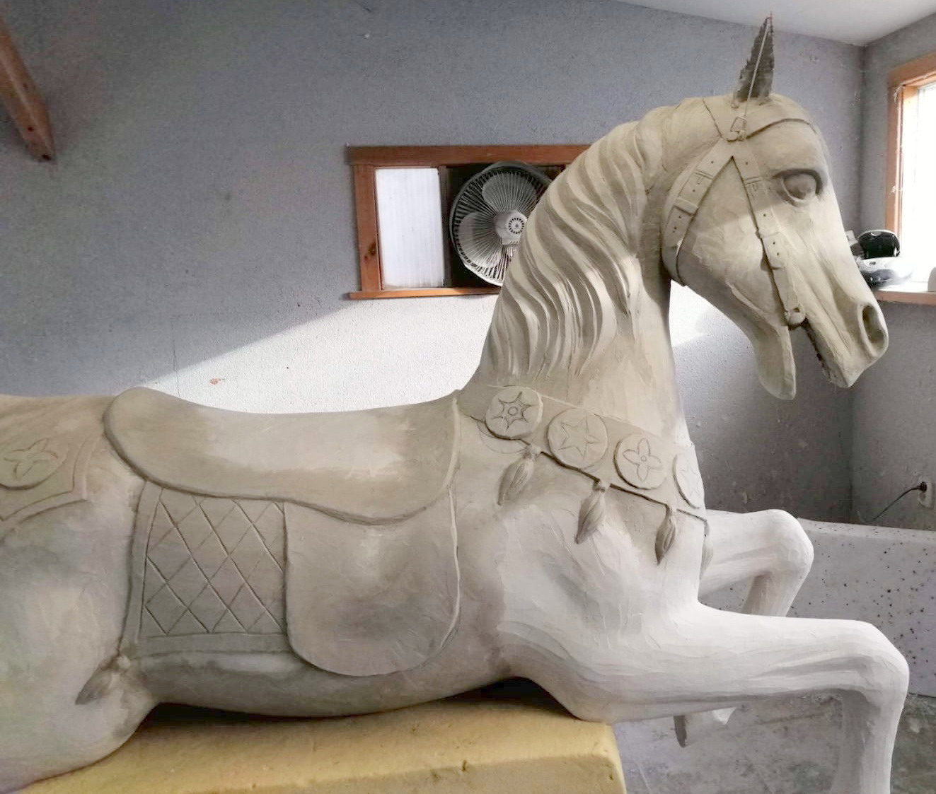 Koń rzeźbiony w drewnie z siodłem i ozdobami w pracowni.