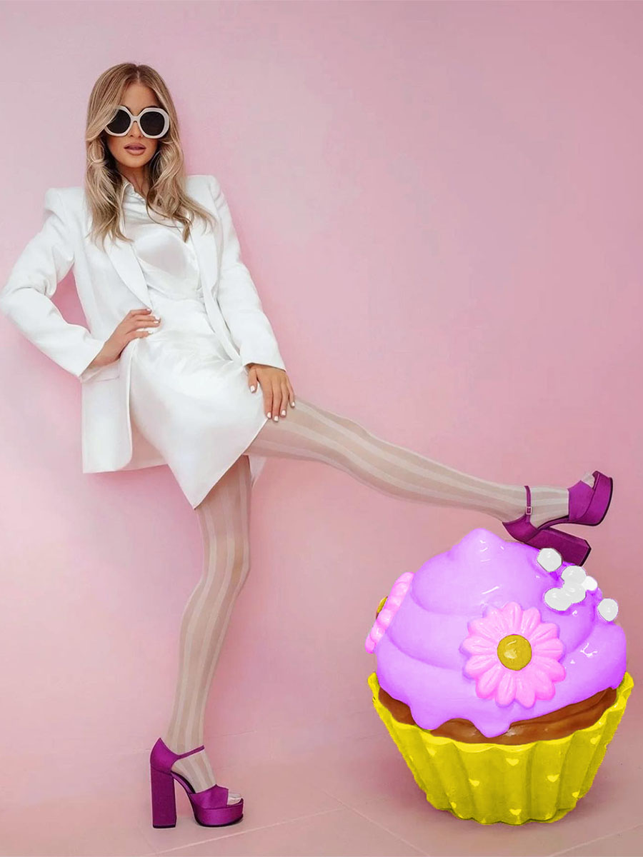 Bunter Cupcake für die Konditorei Sweet Home in Lagos, Portugal. 4 Kobieta w białym stroju, okularach przeciwsłonecznych i fioletowych butach na wysokim obcasie na tle różowej ściany, z fioletowo-żółtą dekoracyjną babeczką.