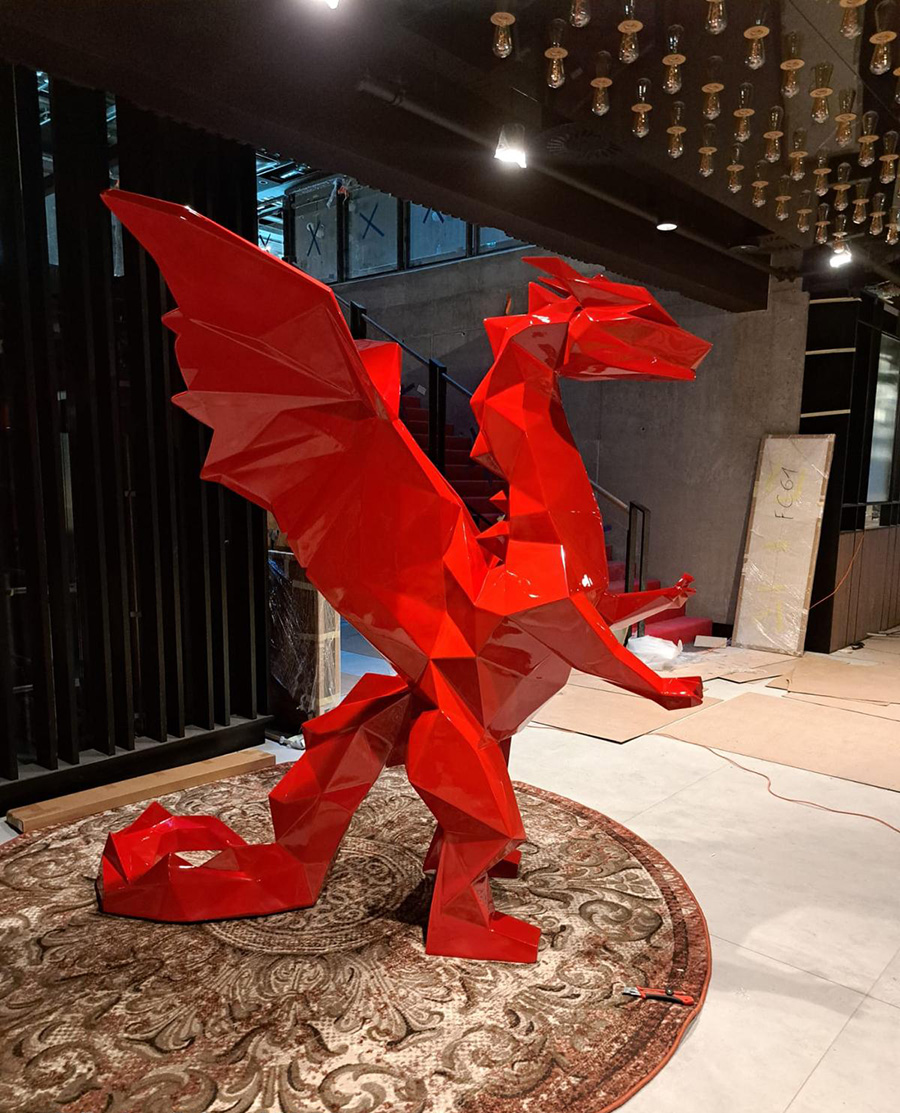 Czerwona, geometryczna rzeźba smoka na ozdobnym dywanie wewnątrz budynku.