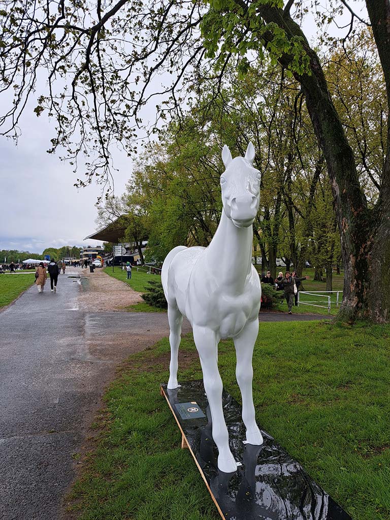 Bunte Pferdeskulpturen auf dem Parcours Partynice in Warschau 3 Biała rzeźba konia stojąca na trawniku w parku.