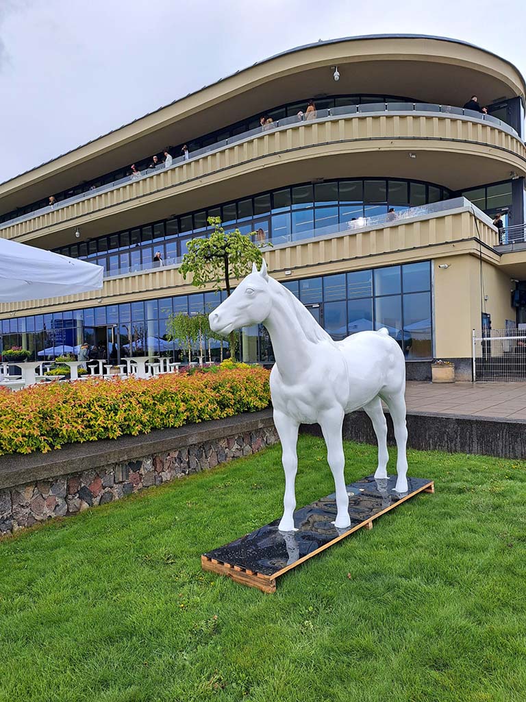 Bunte Pferdeskulpturen auf dem Parcours Partynice in Warschau 1 Biały pomnik konia na trawniku przed nowoczesnym budynkiem z dużymi oknami.