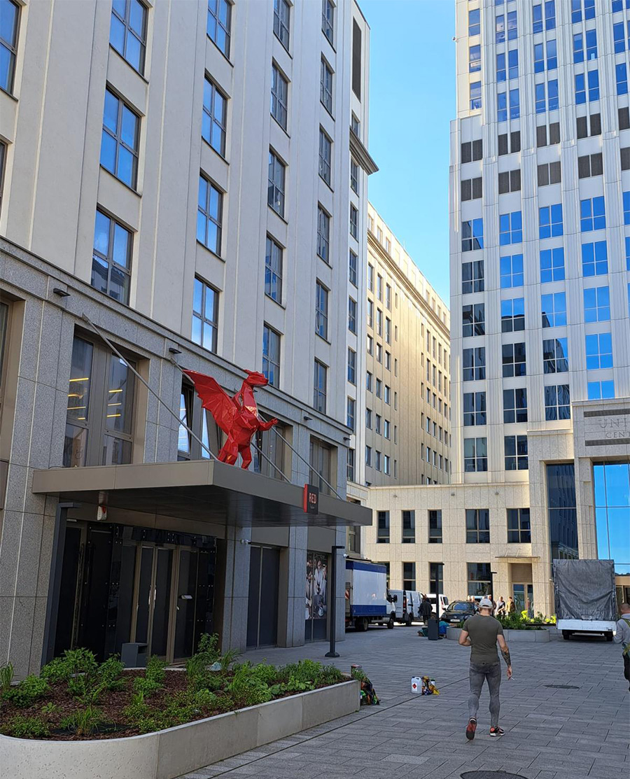 Budynek z czerwoną rzeźbą konia na daszku oraz osoba przechodząca chodnikiem.