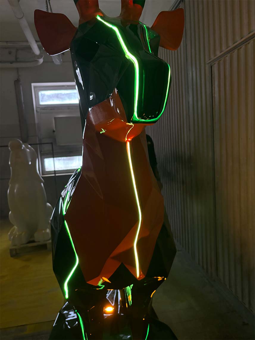 Geometryczna rzeźba żyrafy z neonowymi zielonymi i pomarańczowymi światłami.