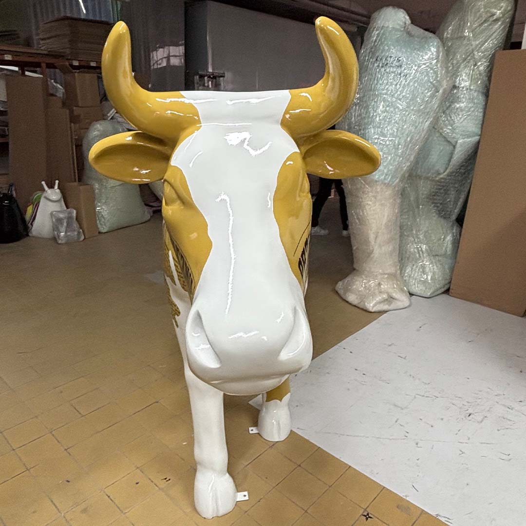 Elektrische Kuh – Symbol der Schlesischen Technischen Universität 7 Figura krowy stojąca na podłodze z żółto-białym malowaniem, w magazynie z owiniętymi w folię przedmiotami w tle