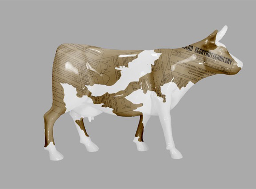 Elektrische Kuh – Symbol der Schlesischen Technischen Universität 2 Model krowy o brązowo-białej skórze z nadrukiem starych dokumentów technicznych na brązowych fragmentach, na szarym tle